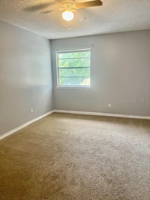 carpeted spare room featuring ceiling fan and a textured ceiling