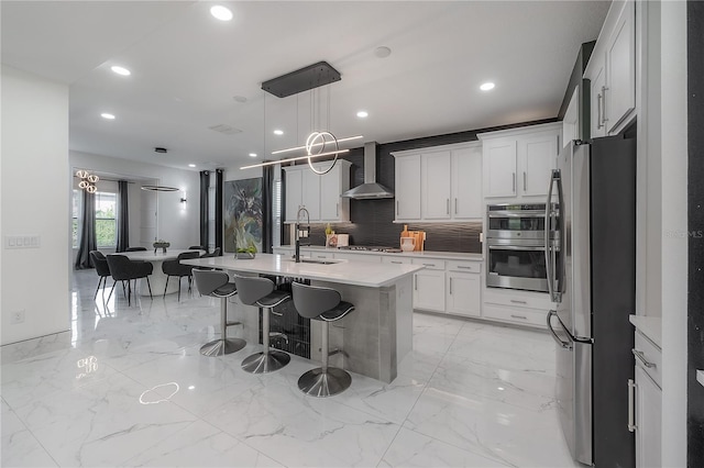 kitchen featuring appliances with stainless steel finishes, a kitchen island with sink, sink, wall chimney range hood, and white cabinetry