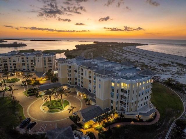 aerial view at dusk featuring a water view and a view of the beach