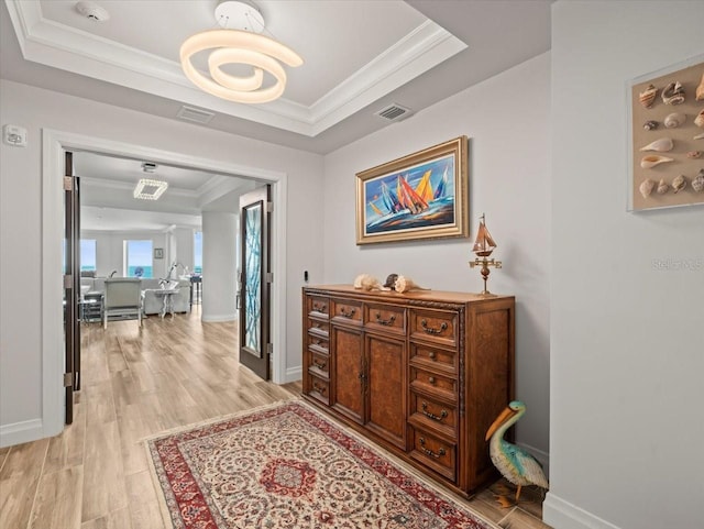 hallway with light hardwood / wood-style floors, ornamental molding, and a tray ceiling