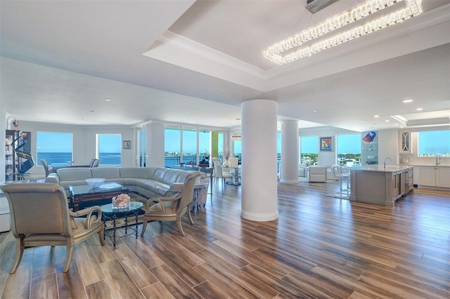 living room with dark hardwood / wood-style flooring, decorative columns, sink, a water view, and a notable chandelier