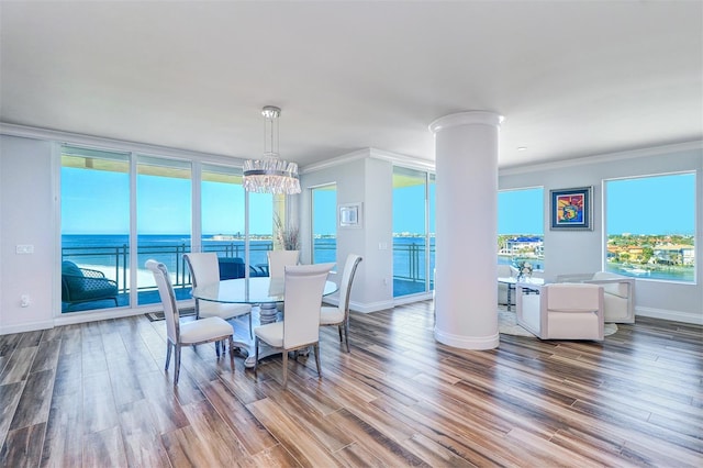 dining space with decorative columns, a water view, wood-type flooring, and ornamental molding