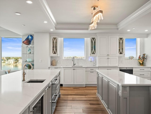 kitchen with backsplash, sink, white cabinetry, and a kitchen island with sink