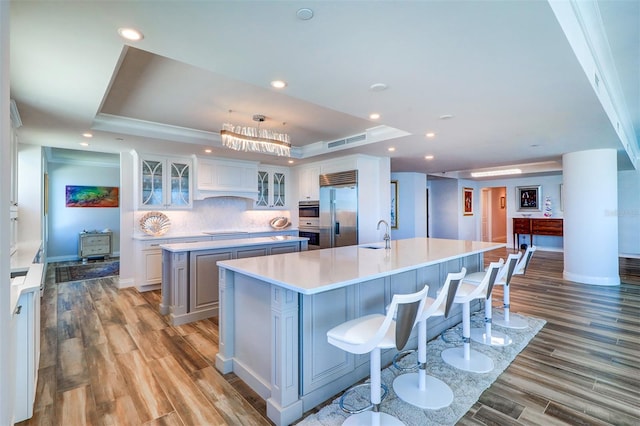 kitchen featuring a large island with sink, light wood-type flooring, a tray ceiling, and appliances with stainless steel finishes