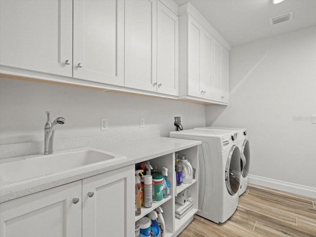 washroom featuring washing machine and dryer, sink, cabinets, and light wood-type flooring