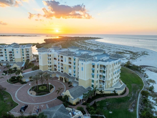 aerial view at dusk featuring a water view and a beach view