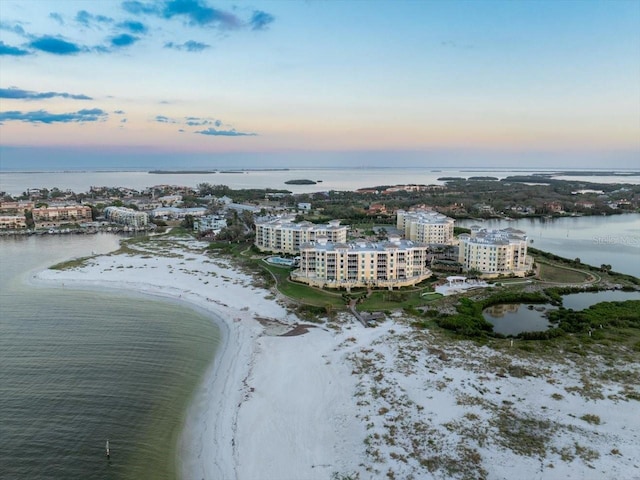 aerial view at dusk featuring a view of the beach and a water view