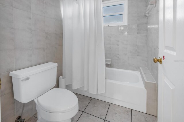 bathroom with tile patterned floors, toilet, shower / bath combo with shower curtain, and tile walls