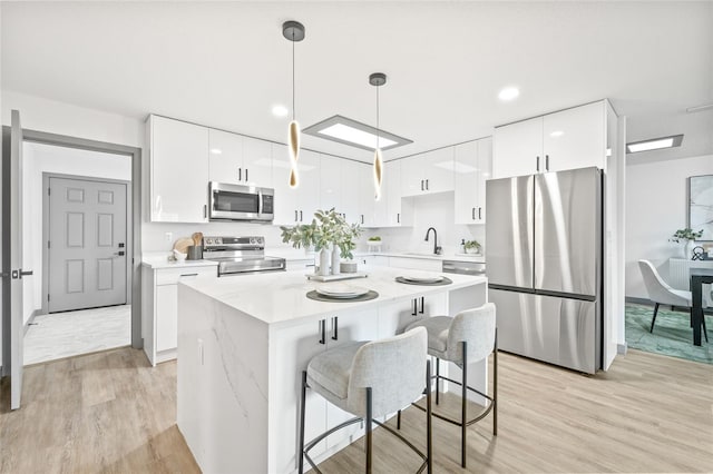 kitchen featuring white cabinetry, stainless steel appliances, decorative light fixtures, and light wood-type flooring