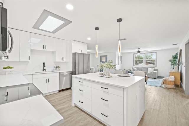 kitchen with appliances with stainless steel finishes, a kitchen island, sink, white cabinetry, and hanging light fixtures