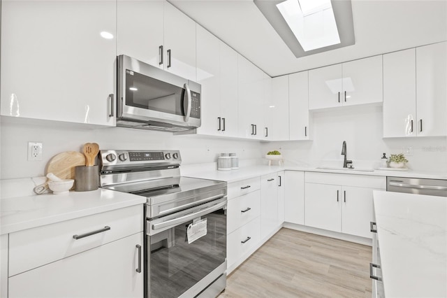 kitchen featuring sink, light stone counters, appliances with stainless steel finishes, white cabinets, and light wood-type flooring