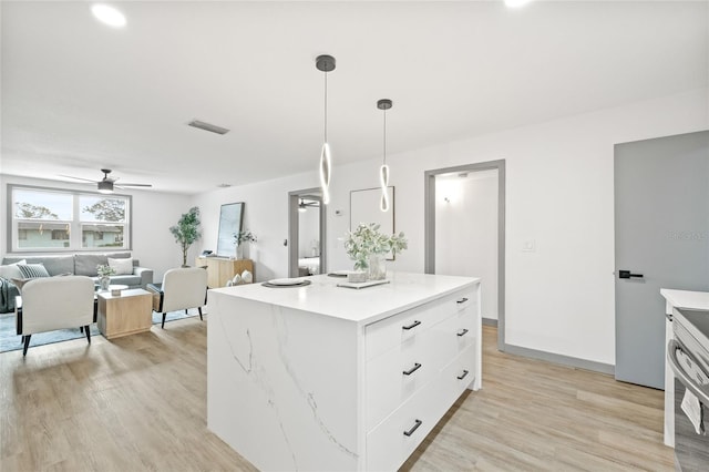 kitchen with ceiling fan, hanging light fixtures, a kitchen island, white cabinets, and light wood-type flooring