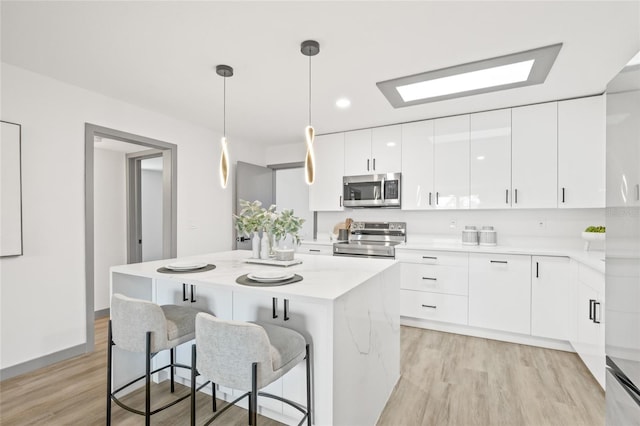 kitchen featuring hanging light fixtures, white cabinets, light hardwood / wood-style floors, a kitchen island, and appliances with stainless steel finishes