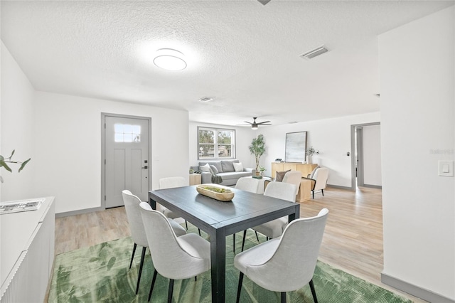 dining room with a textured ceiling, light wood-type flooring, and ceiling fan