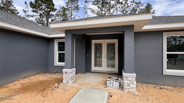 entrance to property featuring a shingled roof, french doors, and stucco siding