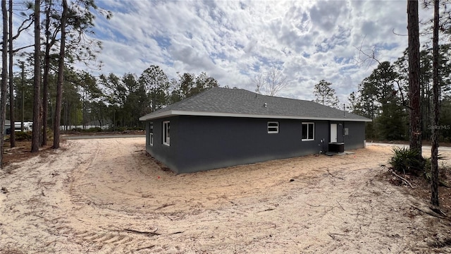 view of property exterior with a shingled roof, central AC unit, and stucco siding