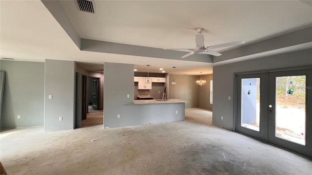 unfurnished living room featuring visible vents, a tray ceiling, french doors, a sink, and ceiling fan with notable chandelier