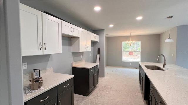 kitchen featuring light stone counters, a sink, white cabinetry, hanging light fixtures, and dark cabinetry