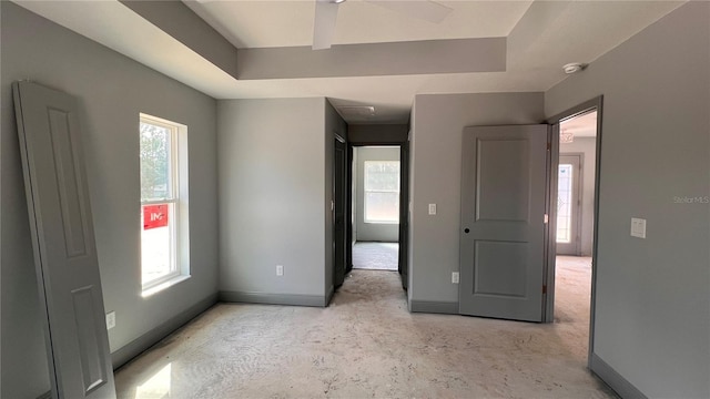 unfurnished bedroom featuring a tray ceiling, unfinished concrete flooring, and baseboards