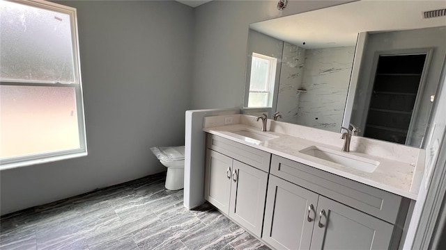 bathroom featuring a marble finish shower, a sink, toilet, and double vanity