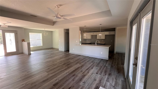 unfurnished living room with baseboards, dark wood-style floors, a tray ceiling, a sink, and ceiling fan with notable chandelier