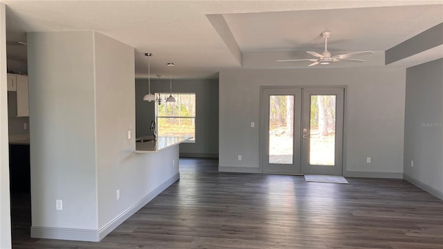 spare room with baseboards, dark wood finished floors, a raised ceiling, ceiling fan, and french doors