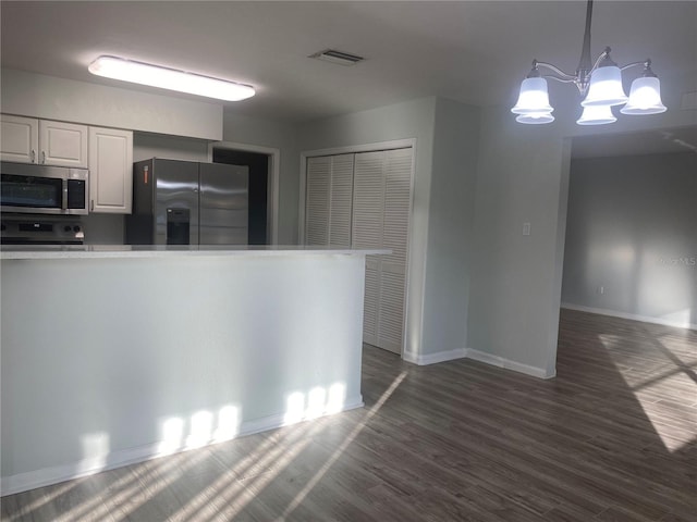 kitchen with pendant lighting, white cabinets, appliances with stainless steel finishes, a notable chandelier, and dark hardwood / wood-style flooring