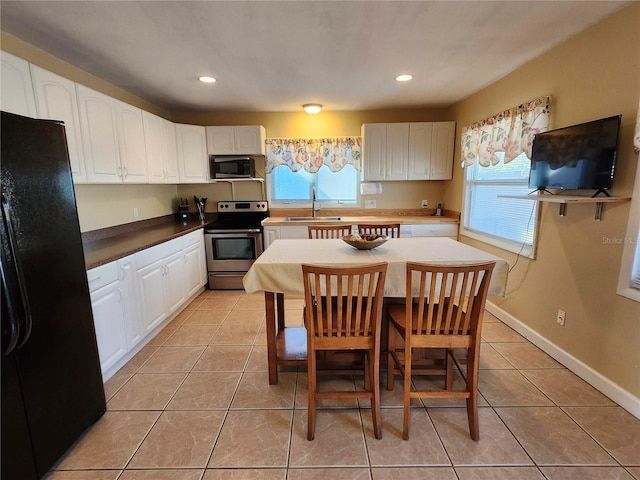 kitchen with baseboards, white cabinets, appliances with stainless steel finishes, a sink, and light tile patterned flooring