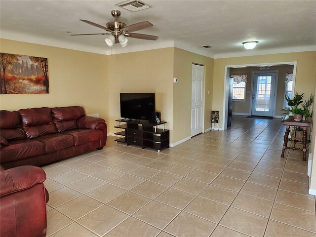 living area with light tile patterned floors, ceiling fan, visible vents, and baseboards