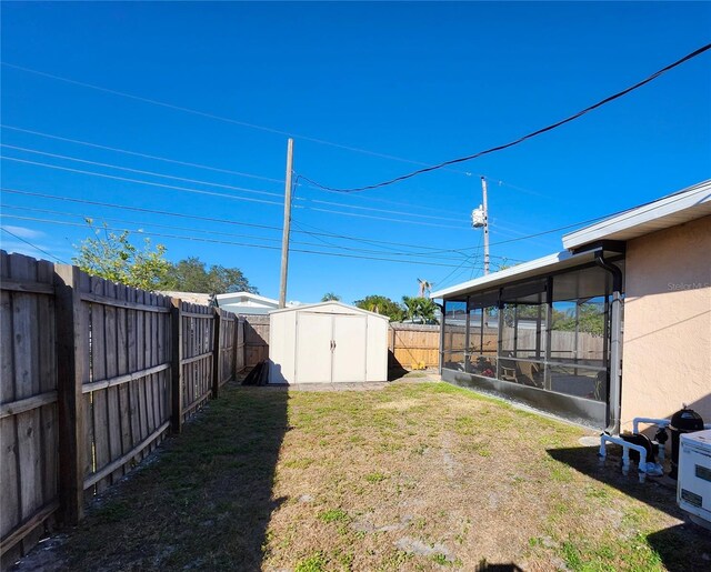 view of yard featuring an outbuilding, a shed, a fenced backyard, and a sunroom