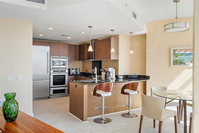 kitchen with pendant lighting, backsplash, a kitchen breakfast bar, built in appliances, and kitchen peninsula