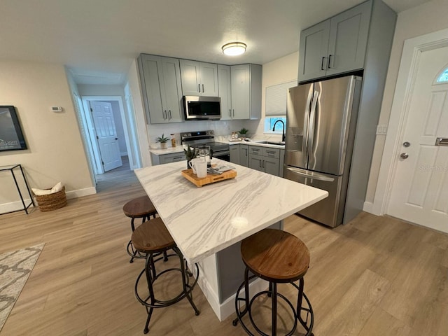 kitchen with a kitchen breakfast bar, gray cabinetry, stainless steel appliances, and light wood-type flooring