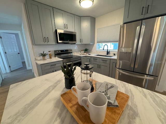 kitchen featuring sink, tasteful backsplash, light hardwood / wood-style floors, light stone counters, and stainless steel appliances