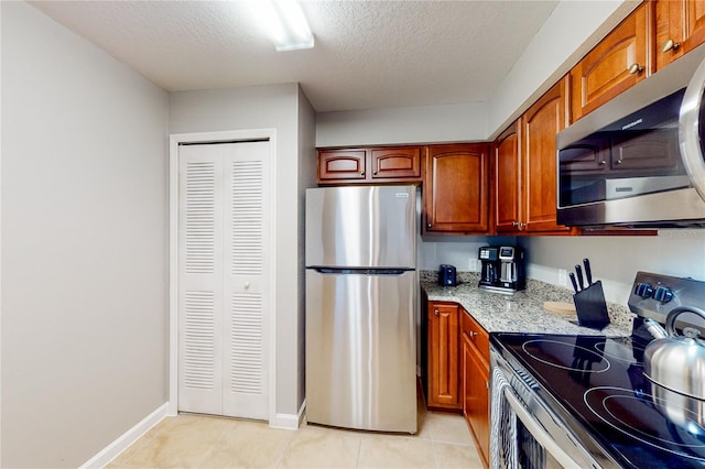 kitchen featuring light stone countertops, appliances with stainless steel finishes, a textured ceiling, and light tile patterned floors