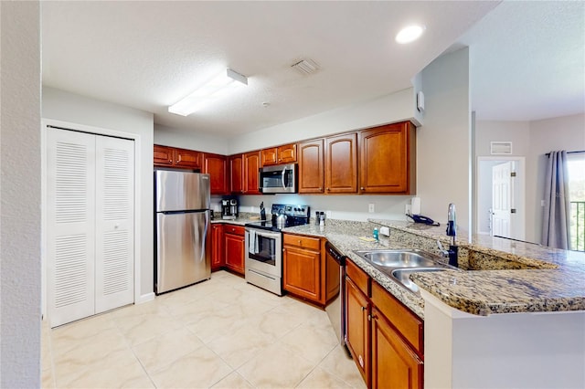 kitchen with kitchen peninsula, appliances with stainless steel finishes, light stone counters, and sink