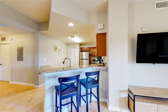 kitchen with stainless steel refrigerator, a kitchen breakfast bar, light stone counters, kitchen peninsula, and electric panel