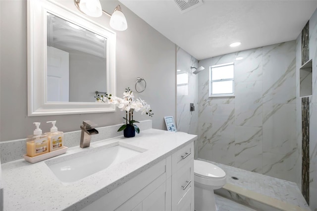 bathroom featuring a tile shower, vanity, and toilet