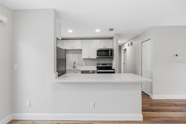 kitchen featuring white cabinetry, light stone counters, light hardwood / wood-style flooring, kitchen peninsula, and appliances with stainless steel finishes