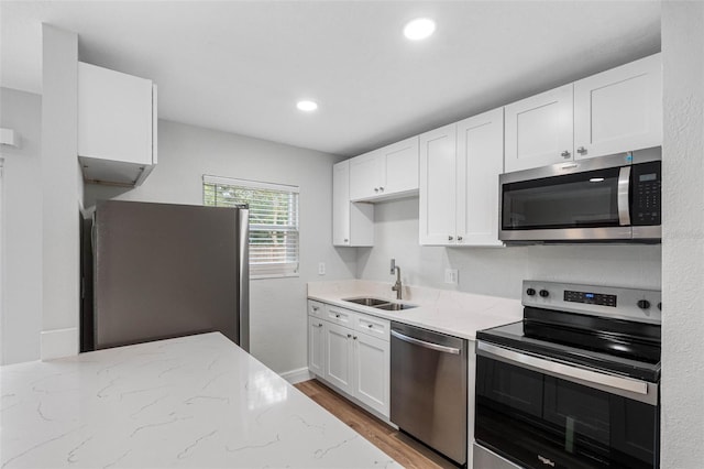 kitchen featuring light wood-type flooring, light stone counters, stainless steel appliances, sink, and white cabinets