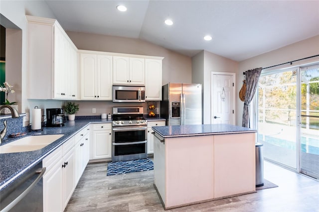 kitchen with lofted ceiling, sink, appliances with stainless steel finishes, a kitchen island, and white cabinetry