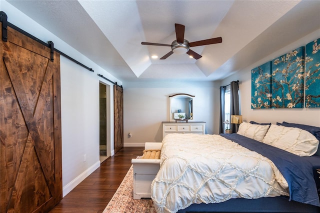 bedroom with a raised ceiling, ceiling fan, a barn door, and dark hardwood / wood-style flooring