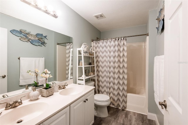 full bathroom with hardwood / wood-style floors, shower / bath combo, vanity, toilet, and a textured ceiling