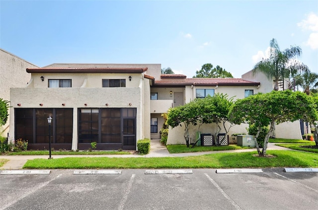 view of front facade with stucco siding, uncovered parking, a front lawn, and a tiled roof