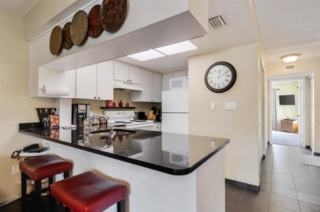 kitchen featuring white appliances, kitchen peninsula, sink, white cabinetry, and a breakfast bar area