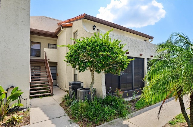 view of side of home with central AC unit, stucco siding, and stairs