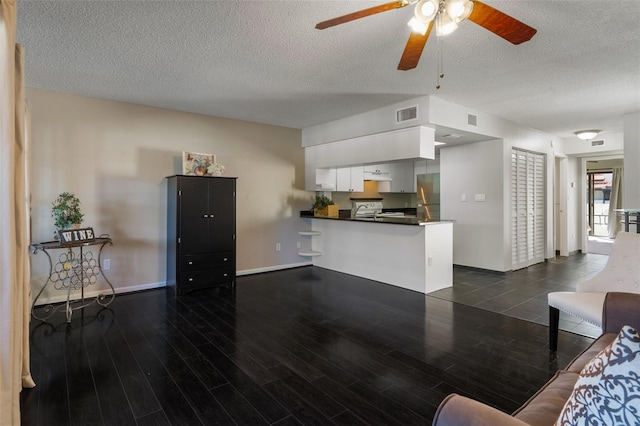 living area featuring dark wood-type flooring, baseboards, visible vents, and a textured ceiling