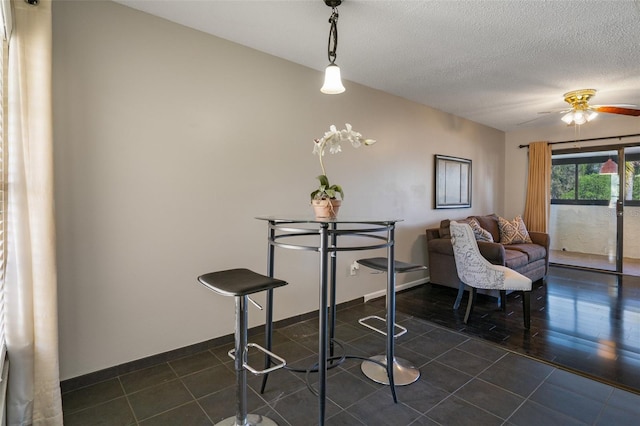 dining area featuring baseboards, dark tile patterned flooring, ceiling fan, and a textured ceiling