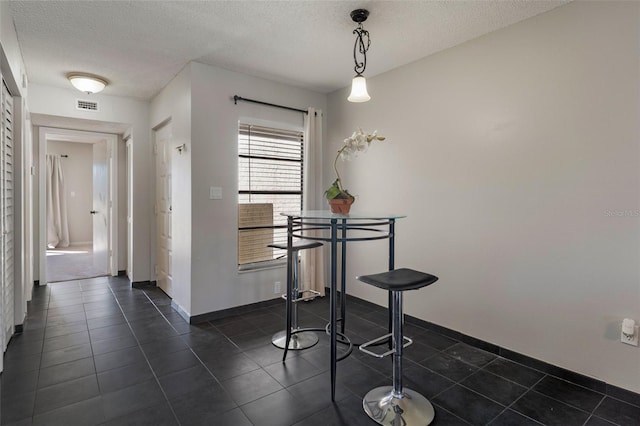 dining room with dark tile patterned floors, baseboards, visible vents, and a textured ceiling