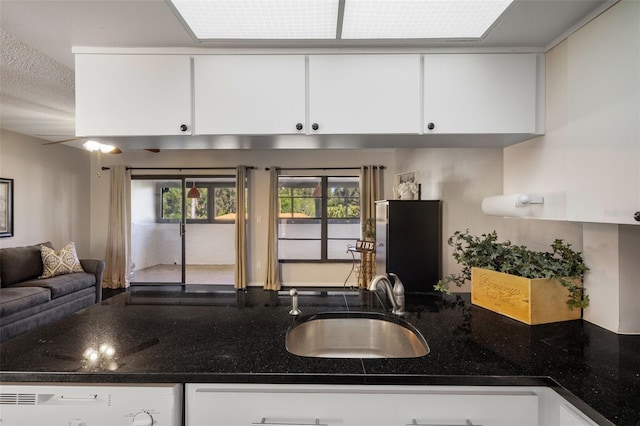 kitchen featuring dark stone counters, a sink, white cabinets, dishwasher, and open floor plan