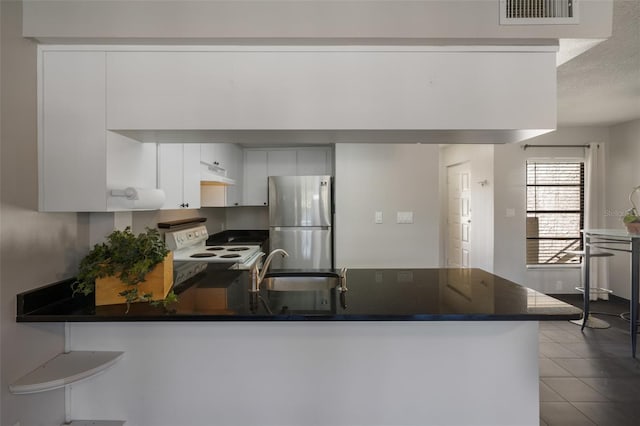 kitchen with visible vents, electric stove, dark countertops, freestanding refrigerator, and a peninsula